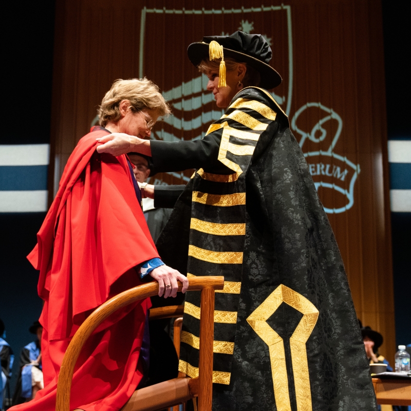 The Governor on one knee to receive a graduation hat from  Australian National University Chancellor Julie Bishop.