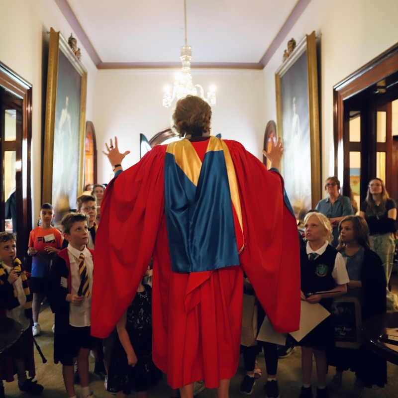 The Governor in a red university gown addressing a crowd of young people at Government House